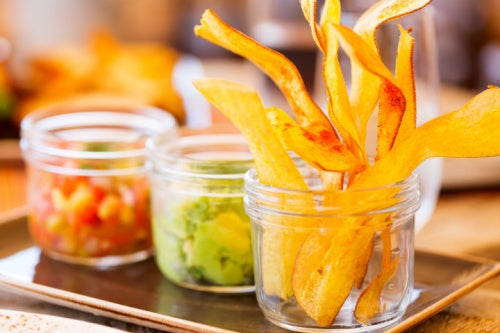 Mariquitas Plantain Chips Con Ajo served in glass jar with salsa and guacamole, snack or appetizer, delicious and colorful